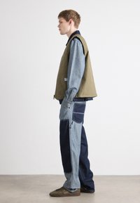 Khaki vest over a blue denim shirt, paired with patchwork denim pants in light and dark shades. Brown sneakers complete the outfit.