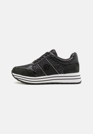 Black sneaker with black laces, suede and textured fabric panels, white and black striped sole, and a circular logo on the side.