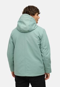 Chaqueta con capucha de color verde menta, con una textura suave, costuras estructuradas y un corte relajado. Diseñada con una capucha amplia y dobladillo recto.
