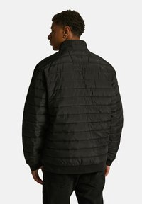 Czarna kurtka puchowa o pikowanej strukturze, z wysokim kołnierzem i ściągaczem na dole. Materiał wydaje się gładki i lekki.