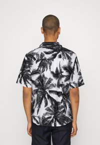 Chemise à manches courtes en tissu blanc ornée d'un motif complet de feuilles de palmier noires, avec une coupe décontractée et un col.