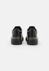 Schwarze Leder-Sneaker mit einem schlanken Design, ausgestattet mit einer dicken schwarzen Sohle und einem goldenen Akzent um die Ferse.