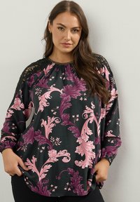 Blusa nera con un motivo floreale rosa e viola, dettagli in pizzo sulle spalle, scollo gather e maniche lunghe. Tessuto morbido, vestibilità ampia.