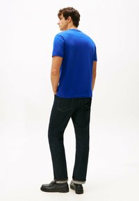 Blå bomulds t-shirt med korte ærmer, parret med mørke denimjeans. Synlige oprevne manchetter og sorte sko. Enkel, afslappet pasform.