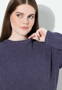 Lila Strickpullover mit einer gerippten Struktur, ausgestattet mit einem runden Ausschnitt und leicht abgesenkten Schultern. Der Stoff wirkt weich und gemütlich.