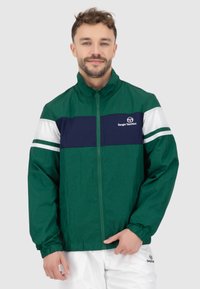 Grüne leichte Jacke mit einem dunkelblauen und weißen horizontalen Streifen auf der Brust. Sie hat einen Stehkragen und einen Reißverschluss sowie einen strukturierten Stoff.
