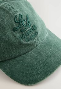 Gorra de béisbol de denim verde con bordado de "LA" y "LOS ÁNGELES California" en hilo a juego, con visera curva y tela texturizada.