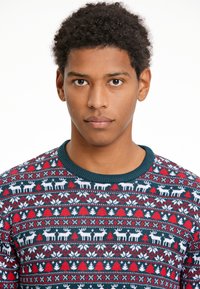 Pārmērnā adīta džempera ar teāla krāsas ribinātu apkakli, ar svētku dizainu, kas ietver sarkanos un baltos ziemeļbriežus, kokus un ģeometriskas formas.