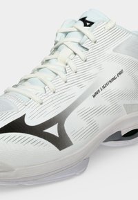 Λευκό αθλητικό παπούτσι Mizuno Wave Lightning Pro με μαύρο λογότυπο, λευκά κορδόνια και υφή στο πάνω μέρος.