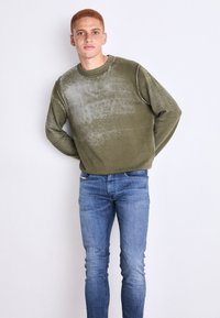 Sudadera de color verde oliva con un ligero degradado, cuello redondo y puños de canalé; combinada con jeans ajustados azules. Textura suave y diseño casual.