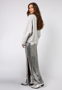 Ezüst flitteres maxi szoknya oldalsó hasítékokkal, szürke túméretű pulóver és fényes ezüst bokacsizma. Sima textúra és tükröződő felületek.