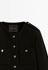 Manteau noir avec encolure arrondie, boutons décoratifs argentés sur les poches avant et épaulette à l'épaule, étiquette Massimo Dutti à l'intérieur du col.