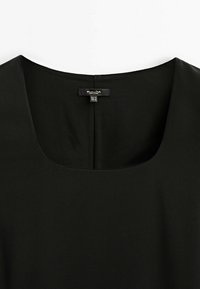 Robe noire à encolure carrée avec une couture centrale au dos, comportant une petite étiquette de vêtement en haut du col arrière.