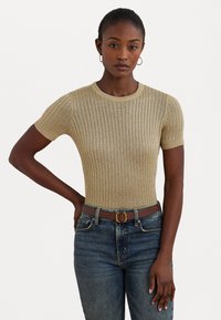 Camisola de manga curta em dourado metálico, com textura canelada. Combinada com jeans de ganga azul e um cinto castanho com fivela dourada.