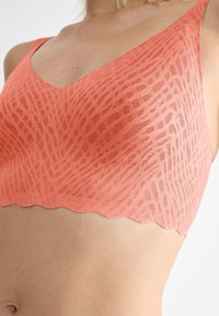 Bralette coral rosa realizzata in tessuto testurizzato con un motivo sottile, design a scollo a V e bordi scallopati per una finitura liscia.
