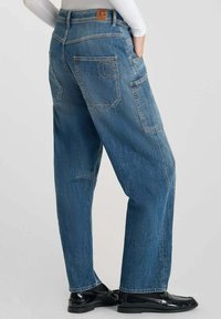 Jeans en denim bleu à jambes larges avec une finition délavée, dotés de poches arrière, de coutures contrastées et d'une étiquette en cuir à la taille.