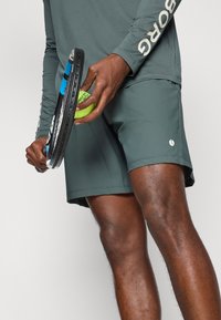 Σκούρο πράσινο αθλητικό σορτς και μπλούζα με μακριά μανίκια. Στην μανσέτα της μπλούζας είναι τυπωμένο το "BORG". Εμφανίζεται μια μαύρη ρακέτα τένις και μια πράσινη μπάλα τένις.