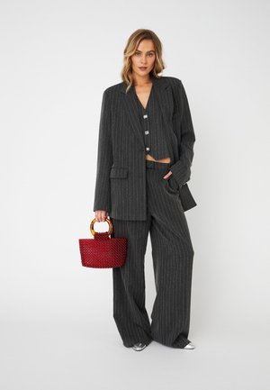 Tummanharmaa pinstripe-puku, johon kuuluu vartalonmyötäinen bleiseri, lyhyt toppi ja leveälahkeiset housut. Asusteena punainen kudottu käsilaukku ja hopeiset kengät.