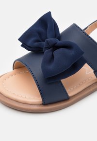 Infradito blu navy con due cinghie e un grande dettaglio a fiocco. Realizzato in materiale sintetico con una soletta beige e una suola marrone.