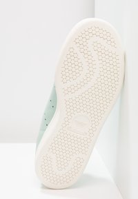 Sneaker verde chiaro con sezioni perforate, suola in gomma bianca con motivo esagonale e logo in rilievo sul tallone.