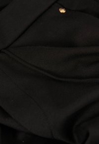 Tissu noir avec une texture lisse, comportant un bouton doré et des coutures visibles, indiquant un design simple et structuré.