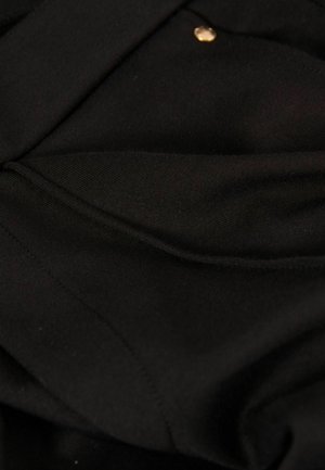 Tissu noir avec une texture lisse, comportant un bouton doré et des coutures visibles, indiquant un design simple et structuré.