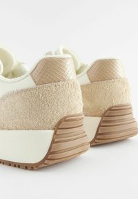 Zapatillas con una parte superior de tela beige claro, paneles de ante marrón texturizado y una suela de goma con detalles estriados.