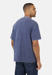 T-shirt in cotone blu con vestibilità rilassata, maniche corte e scollo rotondo. Presenta dettagli di cucitura visibili e una finitura leggermente strutturata.