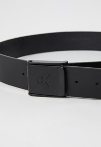 Black leather belt featuring a square black metal buckle with an embossed "CK" logo, and evenly spaced holes along the strap.