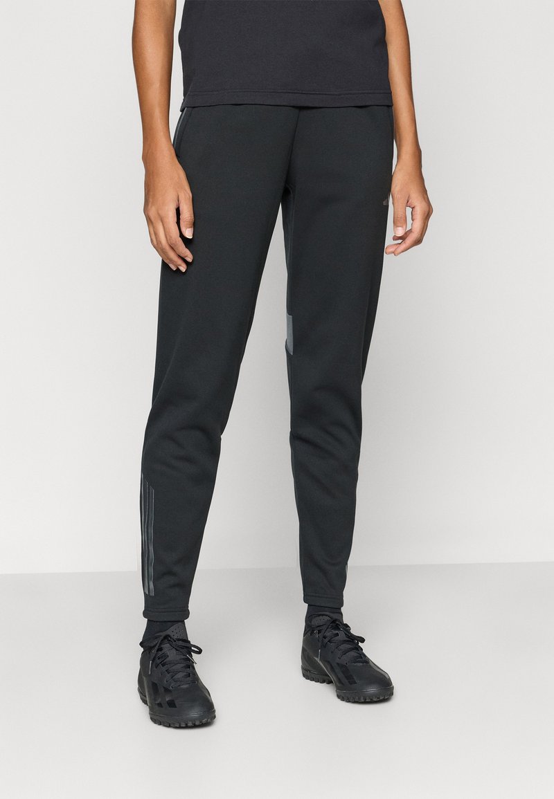 Pantaloni atletici negri cu picioare conice, confecționați dintr-un material neted. Prezintă accente reflectorizante și dungi laterale subtile pe partea inferioară a picioarelor.