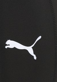 Czarny materiał sportowy o prążkowanej fakturze, z wyraźnym białym sylwetką logo Puma. Wykończenia szwów wzdłuż krawędzi.