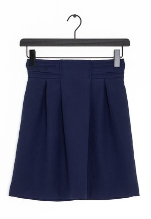 Jupe plissée bleu marine avec large ceinture suspendue sur un cintre en bois noir avec des pinces métalliques sur fond blanc.