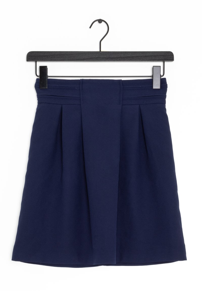 Jupe plissée bleu marine avec large ceinture suspendue sur un cintre en bois noir avec des pinces métalliques sur fond blanc.