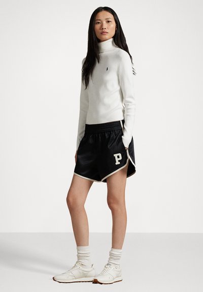 Witte coltrui, zwarte satijnen short met witte bies en 'P' logo, witte sportschoenen en lichte sokken met ribbels.