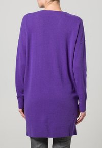 Dlouhý fialový svetr s volným střihem, žebrovanými manžetami a lemem. Měkká textura, kulatý výstřih a spadená ramena pro pohodový vzhled.