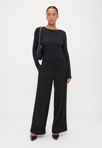 Melnas garas piedurknes bodijs, apvienots ar platām melnām biksēm, kas ir ar gludu tekstūru, salocītām piedurknēm un norādītām melnām kurpēm ar papuče.