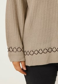 Beige neulepaita, jossa on ribatut hihansuut ja helma. Alareunassa on ruskea timantinmuotoinen kuvio. Pehmeä tekstuuri, rento istuvuus.