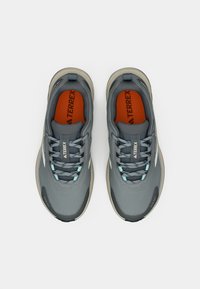 Graue Sportschuhe aus strukturiertem Stoff mit hellblauen Akzenten und einer hellbraunen Gummisohle. Mit Schnürsenkeln und einer orangen Innensohle mit Markenlogo.