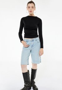 Top negro de manga larga con un diseño ajustado, bermudas de mezclilla azul claro con dobladillo deshilachado y botas de cuero negras hasta la rodilla con hebillas.