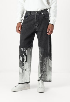 Jeans in denim nero con una stampa fotografica di edifici urbani sulla parte bassa delle gambe. Presentano una vestibilità dritta e cuciture a vista.
