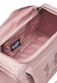 Pink sports duffel bag with a zipper closure, fabric material, smooth texture, large interior, and a small interior pocket with a brand label.
