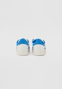 White sneakers with bright blue padded heel collars shown from the back on a plain white background.