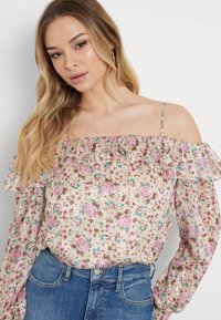 Off-the-shoulder bluse med blomstermønster i pink og blå på en beige baggrund, med flæset ærmer og letvægtsstof.