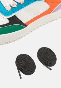Multicolored sneaker featuring textured leather in white, black, green, orange, and purple with two rolled black shoelaces nearby.
