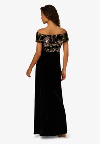 Schwarz samtiges Abendkleid mit einem schulterfreien, mit Perlen verzierten Oberteil, das Blumenmuster zeigt. Lang, fließender Rock, der bis zum Boden reicht.