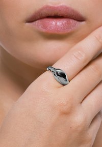 Anello d'argento con un design liscio a forma di foglia; finitura lucida che riflette la luce. Indossato su una mano, che mostra una texture della pelle naturale.