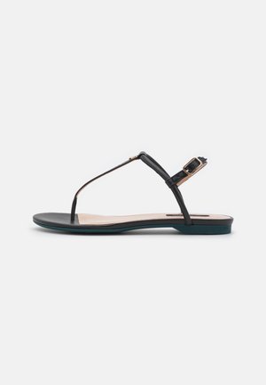 Sort flad sandal med tynde remme, tåpost og justerbar ankelspænde vist i profil på ensfarvet baggrund.