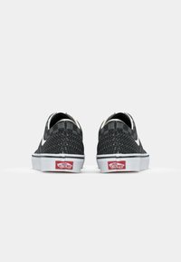 Musta tekstuurilla varustettu Vans-urheilukengät, joissa on valkoiset kumipohjat. Kengissä on kuvioitu kangasmateriaali ja punainen logo kannassa.