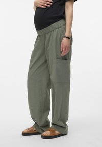 Lichte, olijfgroene zwangerschapsbroek met elastische tailleband, zijzak en loose fit, gecombineerd met bruine slipper sandalen.