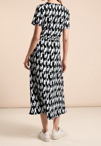 Svart och vit mönstrad midi-klänning med korta ärmar, åtsittande midja och avslappnad passform, ihop med vita sneakers.